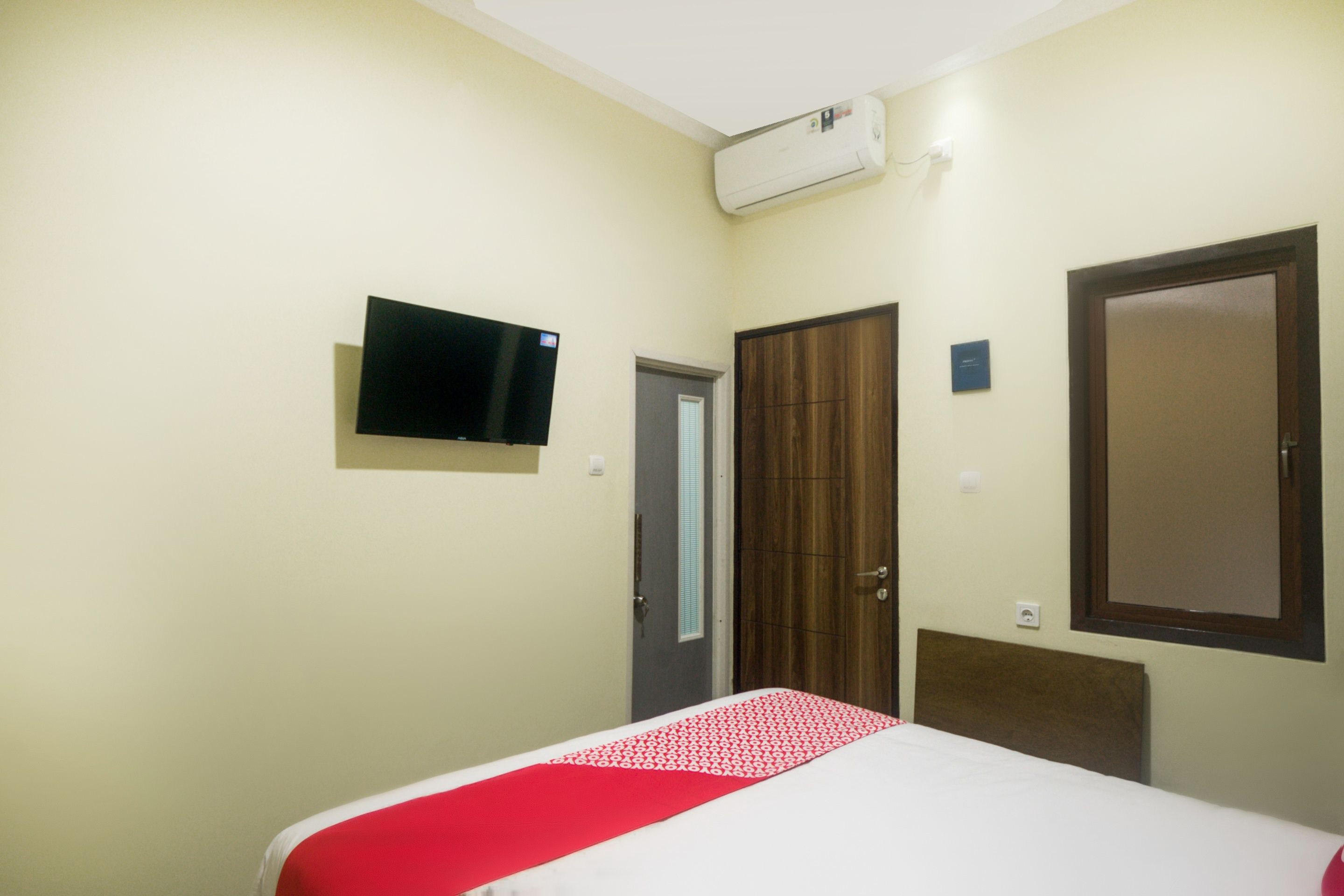 Una habitación de hotel con una cama, televisión montada en la pared, armario y una puerta.