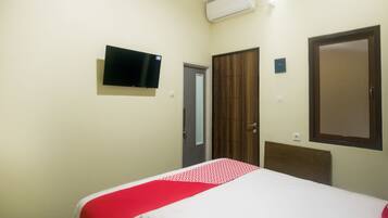 Una habitación de hotel con una cama, televisión montada en la pared, armario y una puerta.
