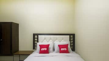 Una habitación de hotel con una cama, dos almohadas rojas con la palabra 'OYO', un armario de madera y una mesita de noche.