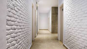 A hallway with white brick walls and a beige floor, leading to a door at the end.