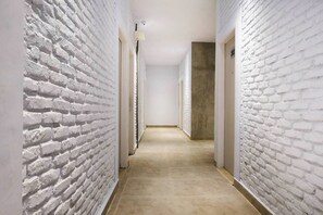 Un pasillo con paredes de ladrillo blanco y piso color beige, que lleva a una puerta al final.