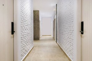 Un pasillo con paredes de ladrillo blanco y piso de baldosas, que conduce a una puerta al final.