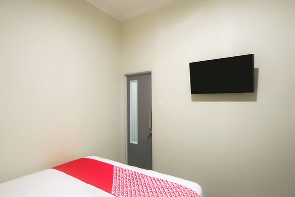 Une chambre d’hôtel avec un lit, une porte et un téléviseur à écran plat fixé au mur.
