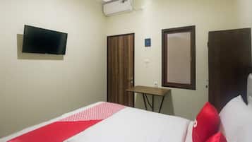 A hotel room with a bed, a TV mounted on the wall, a wooden wardrobe, and a small table.