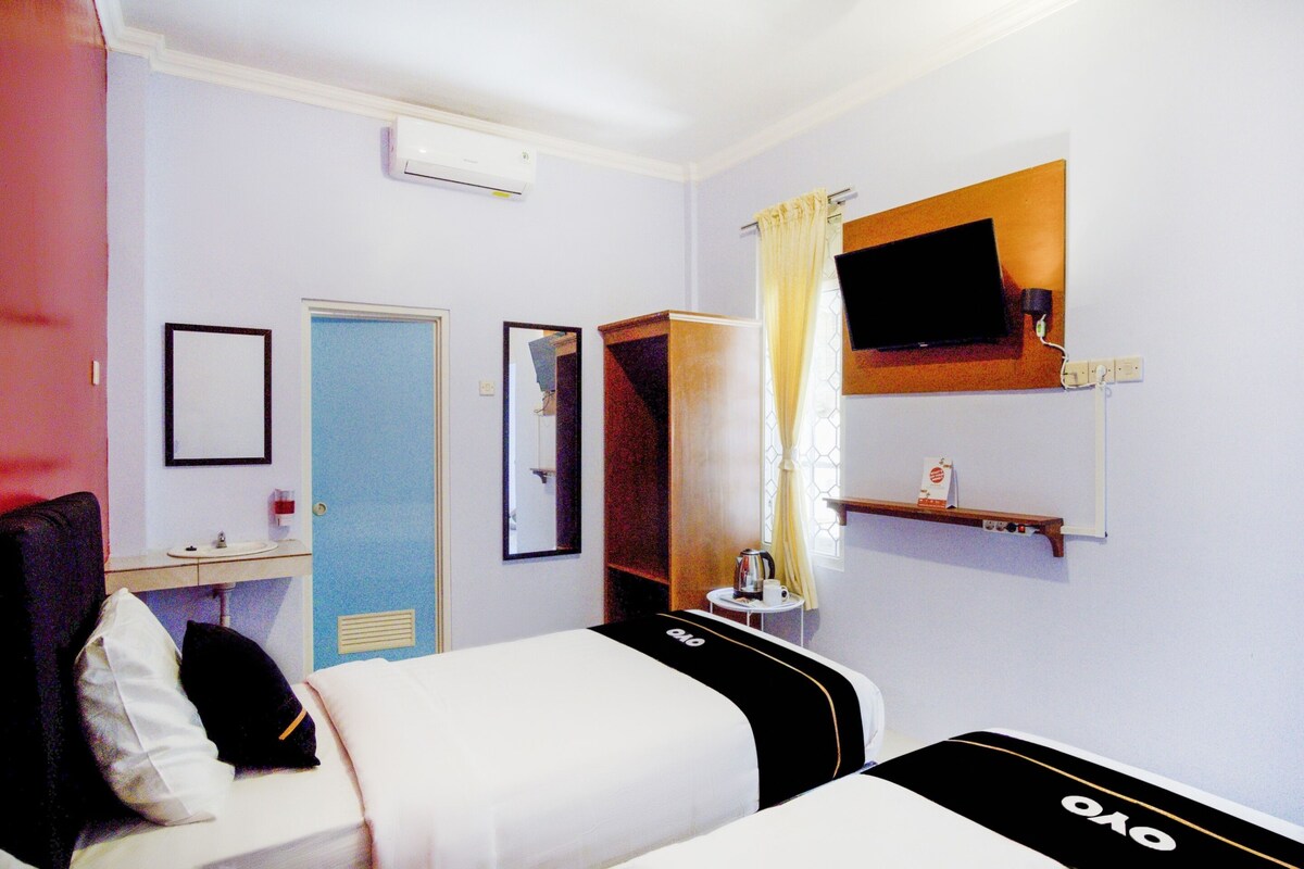A hotel room with a bed, a bedside table, a mirror, a TV mounted on the wall, and a window with curtains.
