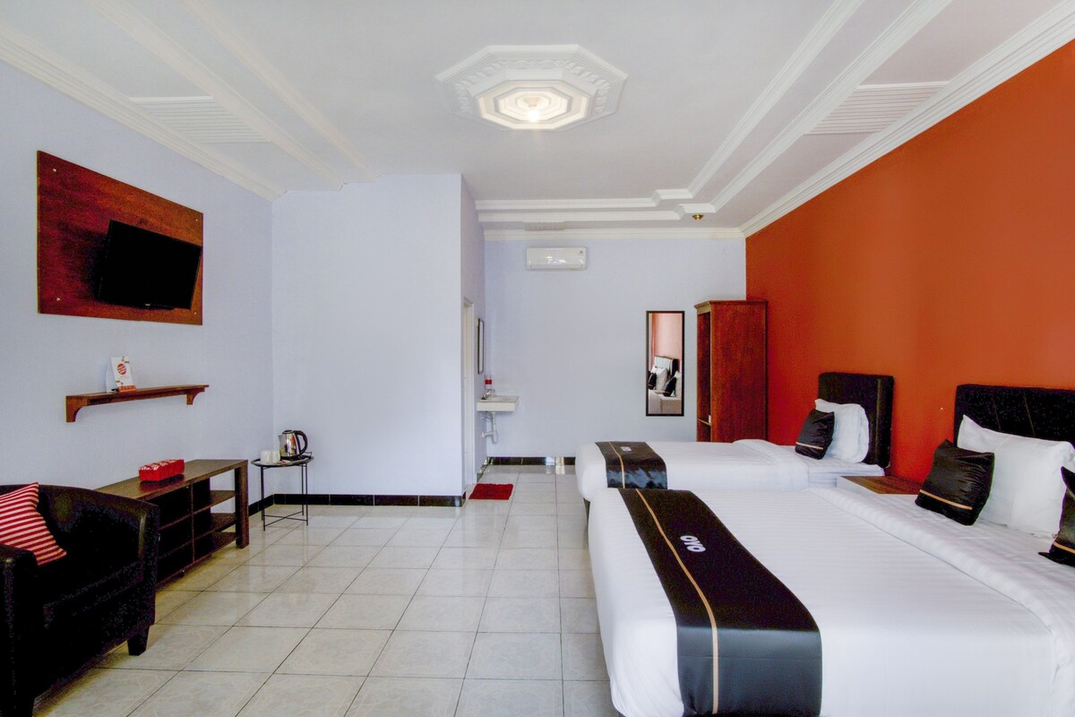 Hotelkamer met twee bedden, een aan de muur bevestigde televisie, een klein tafeltje met een waterkoker en een rood vloerkleed.