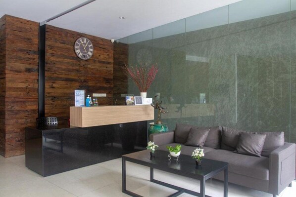 A modern reception area with a wooden wall, a reception desk, a sofa, and a coffee table. - OYO 3931 Wtc Kuningan (Jakarta)