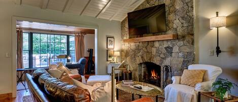 Ett mysigt vardagsrum med en steneldstad, en lädersoffa och en tv som är monterad på väggen.