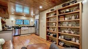 Eine gemütliche Küche mit Holzausstattung, einem Edelstahlkühlschrank und einem großen Regal voller Geschirr und Gläser.
