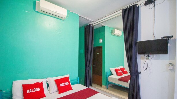 Ein Hotelzimmer mit Türkiswänden, einem Bett mit roten Kissen, einem Wandfernseher und einer Schiebetür zu einem Badezimmer.