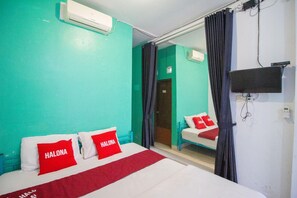 Hotelkamer met turquoise wanden, een bed met rode kussens, een televisie aan de muur en een schuifdeur naar een badkamer.