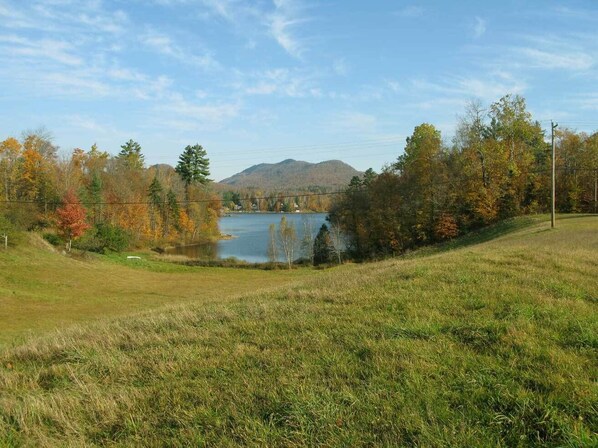 A grassy field with a lake and mountains in the background.