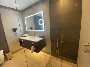 A modern bathroom with a large mirror, two sinks, a shower, and a towel rack.
