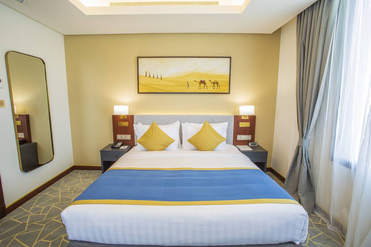 Een hotelkamer met een groot bed, twee nachtkastjes, een spiegel en een schilderij van een woestijnlandschap.