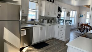 A modern kitchen with white cabinetry, stainless steel appliances, and a view of the ocean through the windows. - Stunning Ocean View Vacation Home, Trinity NL (Trinity)
