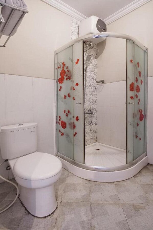 A bathroom with a glass shower enclosure, a toilet, and a white tiled floor. - 3935 Artha Ambarukmo Exclusive (Depok)