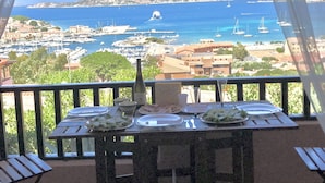 Ein Balkon mit Esstisch, mit Blick auf einen Yachthafen und eine Küstenstadt.
