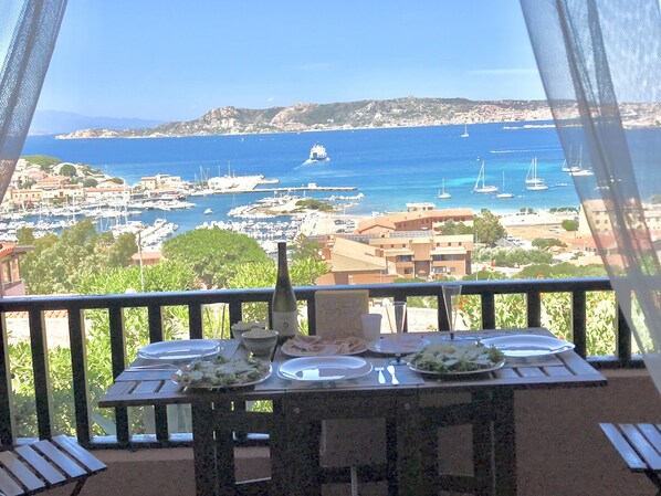Un balcone con tavolo apparecchiato per mangiare, con vista su una marina piena di barche e una cittadina costiera.