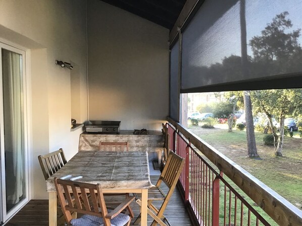 A covered outdoor dining area with a table and chairs, a grill, and a view of the surrounding area.