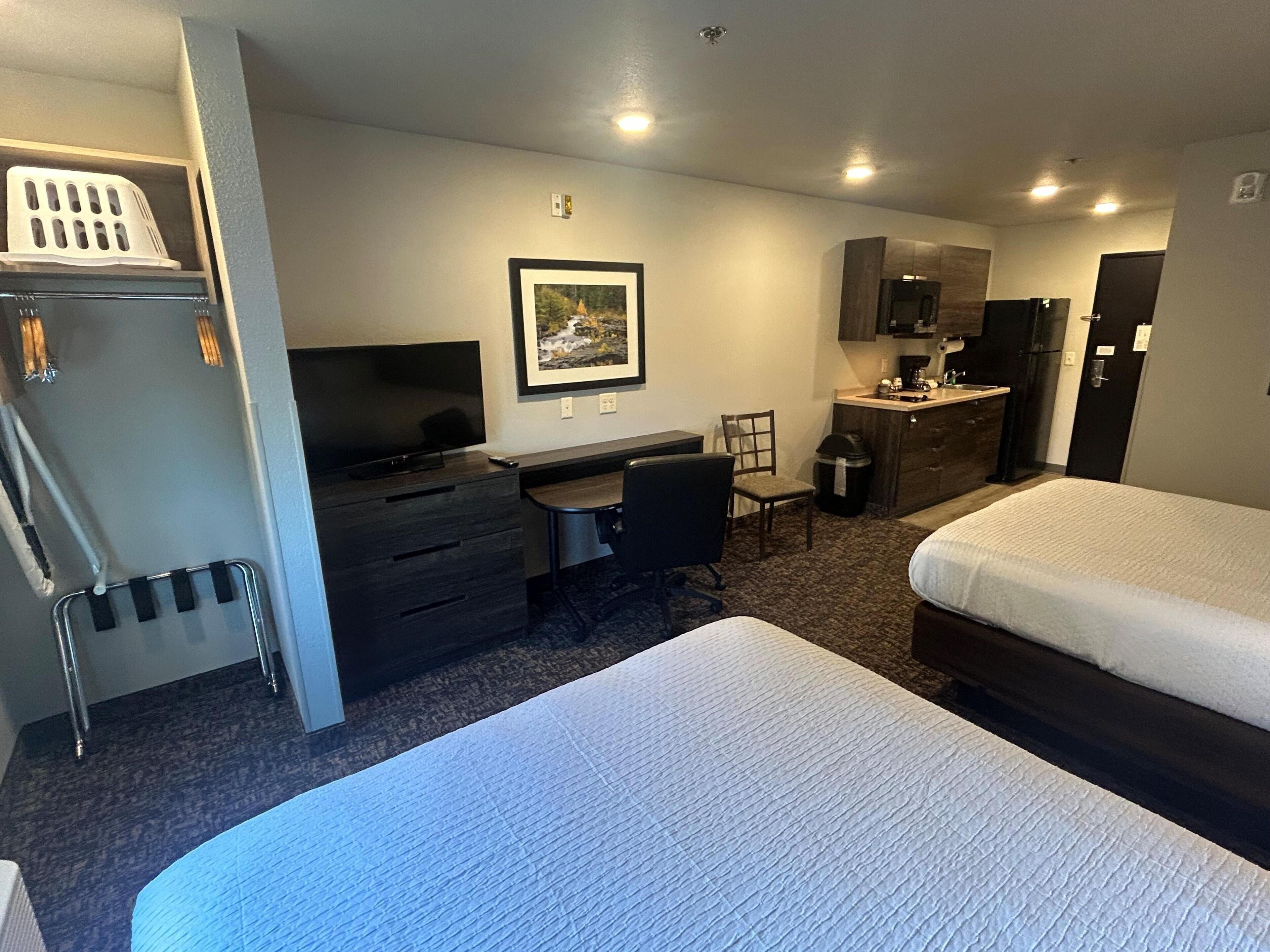 A hotel room with a bed, a desk, a chair, a television, a picture on the wall, and a kitchenette.