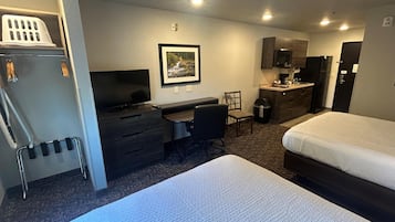 A hotel room with a bed, a desk, a chair, a television, a picture on the wall, and a kitchenette.