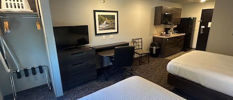 A hotel room with a bed, a desk, a chair, a television, a picture on the wall, and a kitchenette.