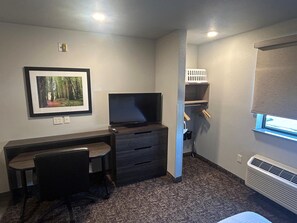 A compact room with a desk, chair, television, and a framed picture on the wall.