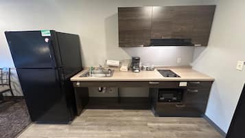 A compact kitchen with a refrigerator, sink, coffee maker, and built-in microwave.
