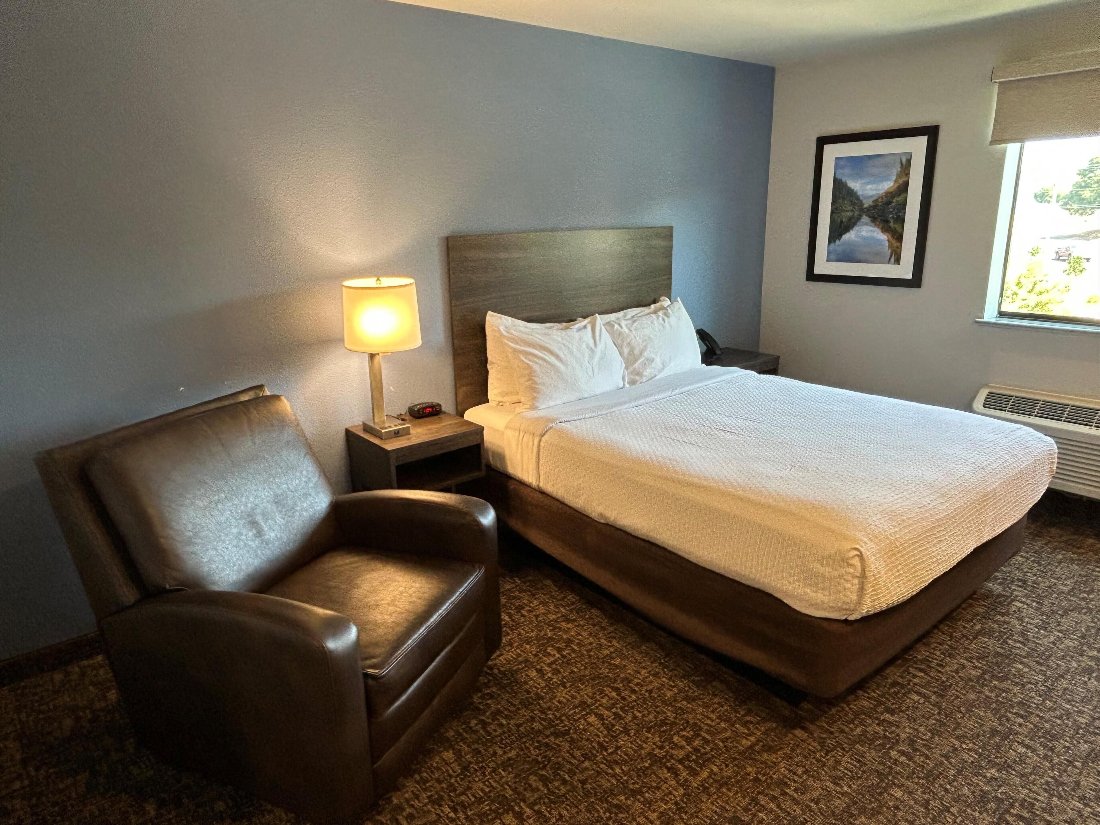 A hotel room with a bed, a chair, a nightstand with a lamp, and a picture on the wall.