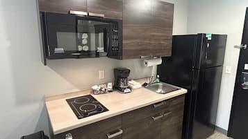A compact kitchen with a microwave, stove, coffee maker, and a refrigerator.