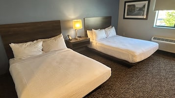 A hotel room with two beds, a nightstand with a lamp, a framed picture on the wall, and a window with a view.