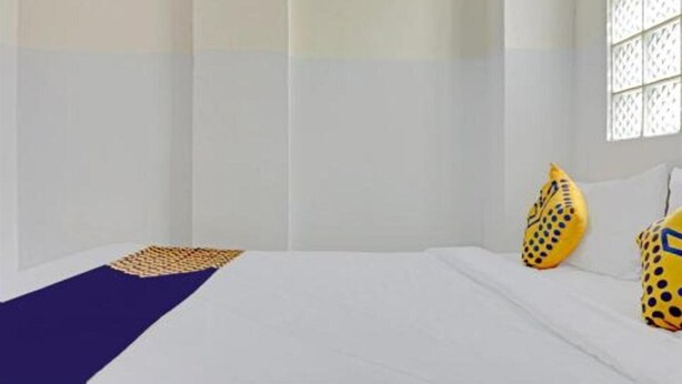 A hotel room with a bed, a window with a lattice design, and two yellow pillows with black patterns. - OYO 4001 Kalideres Residence Syariah (Jakarta)