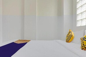 Habitación de hotel con cama, ventana de celosía y dos almohadas amarillas con diseños negros.