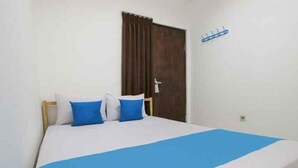 A single bed with a blue bedspread and two pillows, a wooden headboard, a brown door, and a wall-mounted hook. - OYO 4001 Kalideres Residence Syariah (Jakarta)