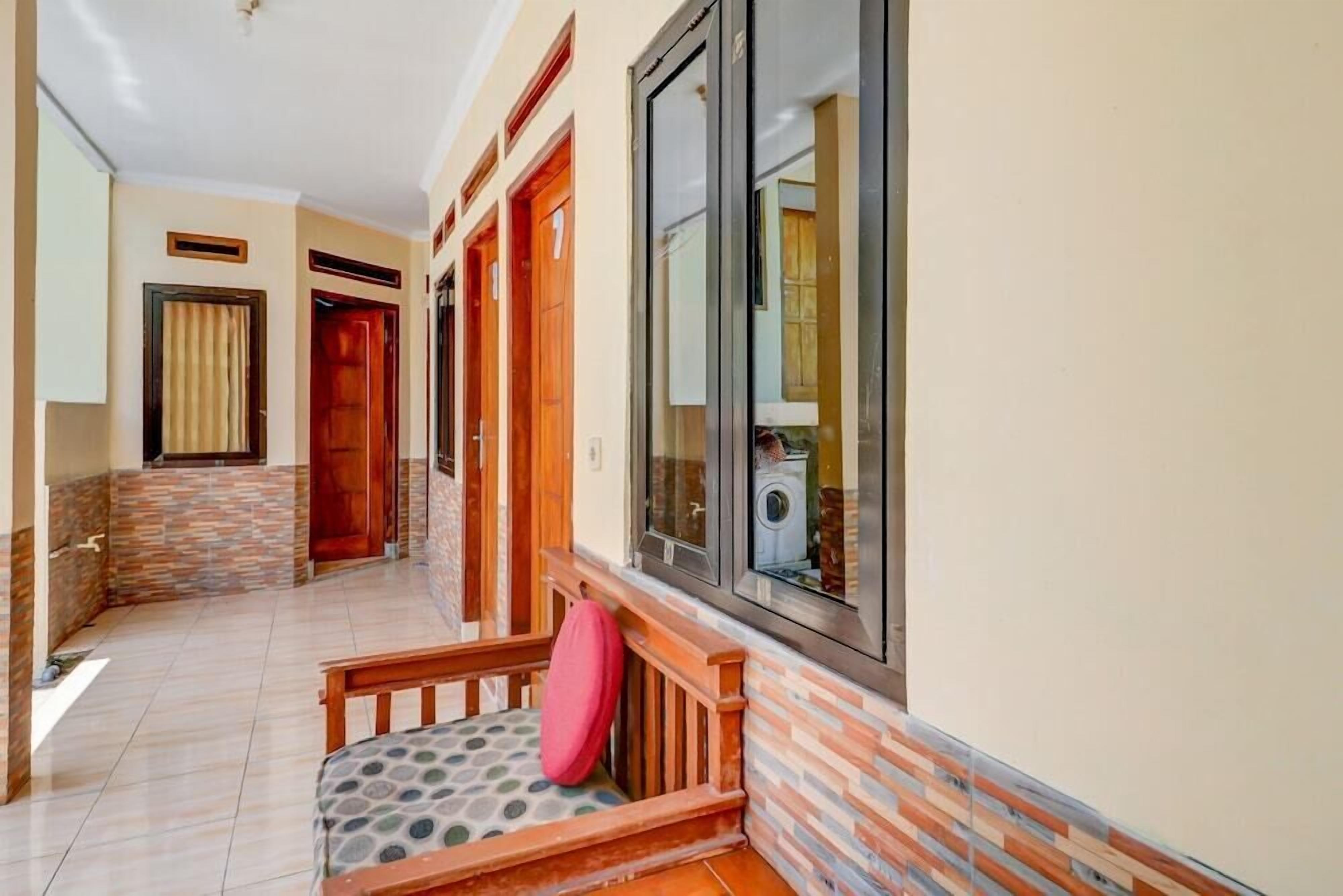 A hallway with a bench, a window with a view of a washing machine, and a door with a number.