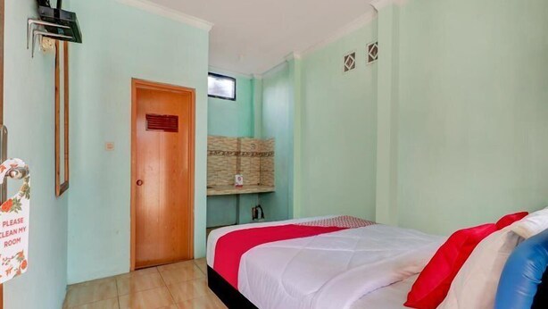 A room with a bed, a television, a door, and a sign on the wall. - OYO 3879 Villa Sari Intan (Ciater)