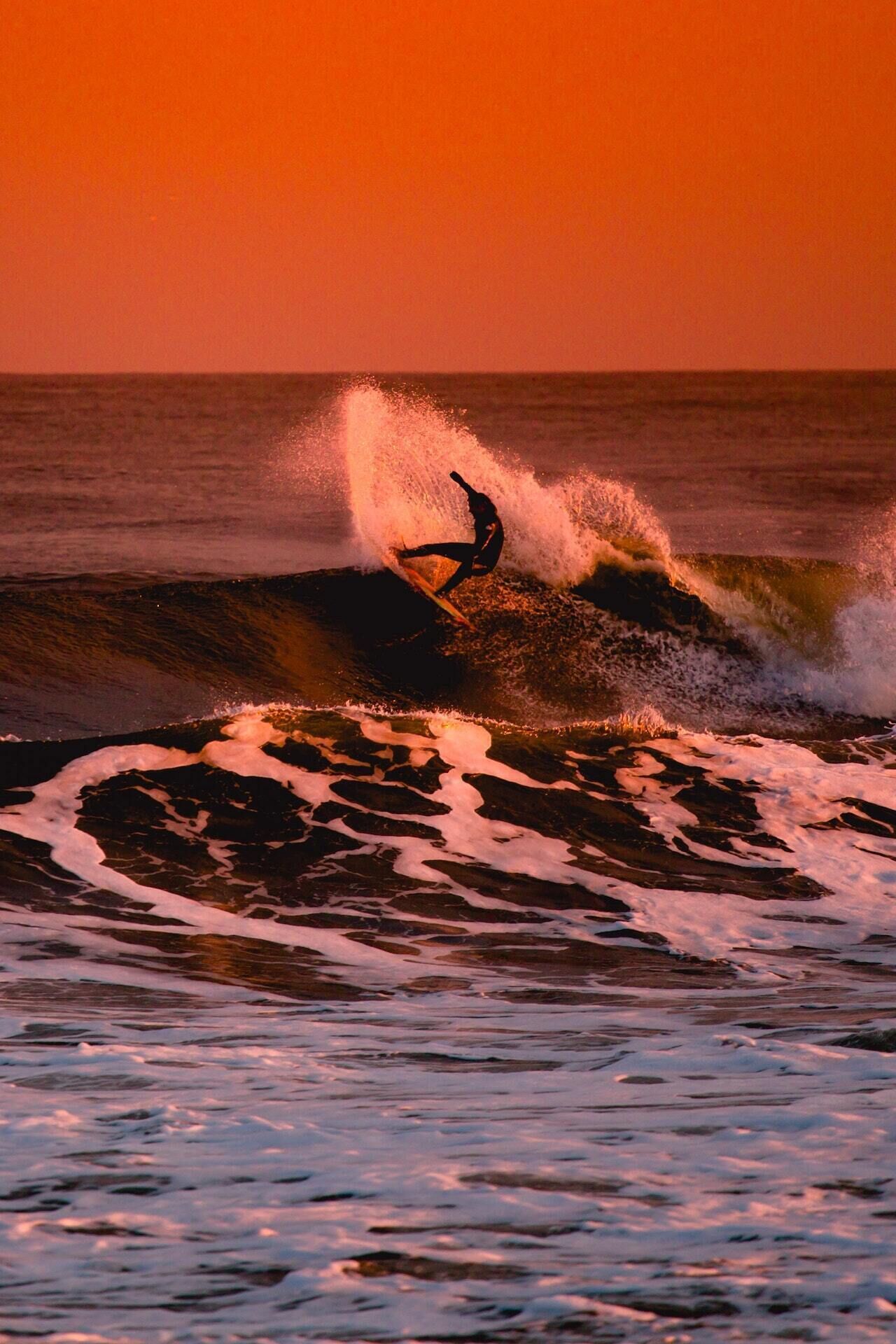 A surfer riding a wave at sunset.
