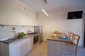 Eine moderne Küche mit Edelstahlgeräten, ein Essbereich mit Tisch und Stühlen sowie ein an der Wand befestigter Flachbildfernseher.