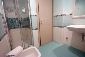 Ein Badezimmer mit einer Duschkabine, einem weißen Waschbecken und einer Tür mit Lichtschalter.