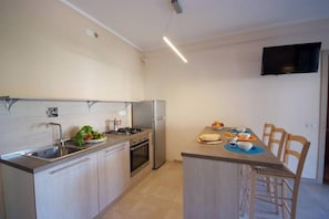 Eine moderne Küche mit Edelstahlgeräten, ein Essbereich mit Tisch und Stühlen sowie ein an der Wand befestigter Flachbildfernseher.