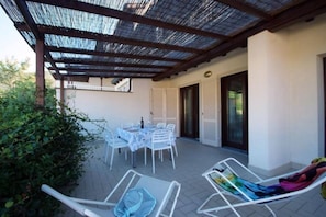 An outdoor patio with a table and chairs, a covered seating area, and a door leading to an interior space.