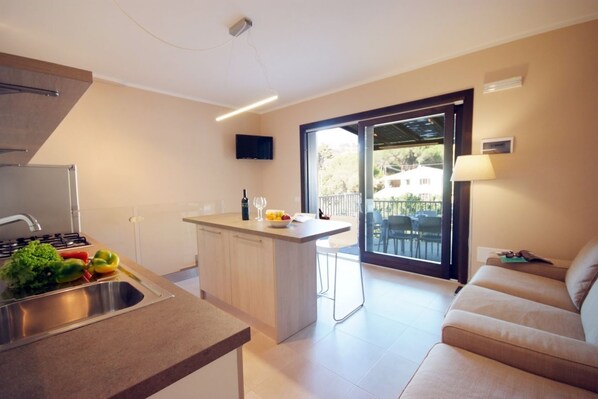 A modern kitchen with a central island, a dining area with a sofa, and a large sliding glass door leading to an outdoor area. - Located just 200 meters from Procchio’s main street and about 600 meters from the beautiful sandy beach, this spacious four-room apartment is the ideal choice for anyone looking for a comfortable and relaxing vacation just a few minutes’ walk from the sea (Procchio)