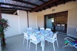An outdoor patio with a table set for four, white chairs, a covered area with a wooden ceiling, and a sliding glass door leading to an interior space. - Located just 200 meters from Procchio’s main street and about 600 meters from the beautiful sandy beach, this spacious four-room apartment is the ideal choice for anyone looking for a comfortable and relaxing vacation just a few minutes’ walk from the sea (Procchio)