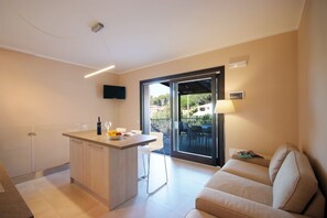 A modern kitchen with a central island, a dining area with chairs, a sofa, and a sliding glass door leading to an outdoor patio.