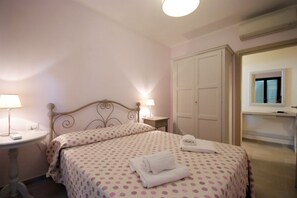 Quarto com cama, luminárias de cabeceira, armário e uma pequena mesa.