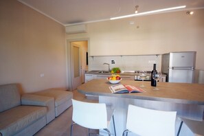 A modern kitchen with a central island, white chairs, and a sofa. - Located just 200 meters from Procchio’s main street and about 600 meters from the beautiful sandy beach, this spacious four-room apartment is the ideal choice for anyone looking for a comfortable and relaxing vacation just a few minutes’ walk from the sea (Procchio)