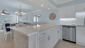 A modern kitchen with white cabinetry, a stainless steel dishwasher, and a large island with a light-colored countertop.