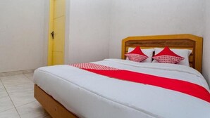 A small, neatly made bed with a wooden headboard, white bedding, and red pillows. - OYO 3060 Al Fatih Guest House Syariah (Tegal)