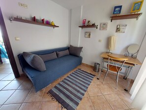 Un salon avec un canapé bleu, un tapis à rayures, un petit bureau et des étagères remplies de divers objets.