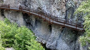 A metal bridge over a rocky cliff with a stream below.